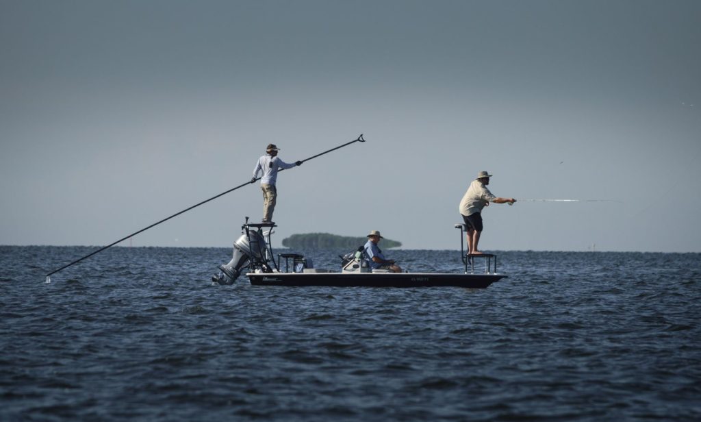 a picture of a flats boat with a captain poling the skiff into position for the angler on the deck while targeting redfish